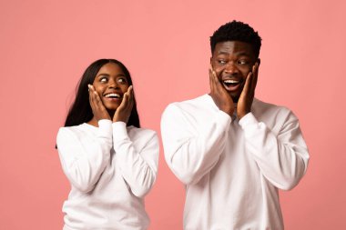 Beyaz eşofman altı giyen Afro-Amerikan erkek ve kadın parlak pembe arka planda sürpriz ve neşe gösteriyor. Elleriyle hareket ederler ve birbirlerine gülümserler, bir anlık heyecanı paylaşırlar..