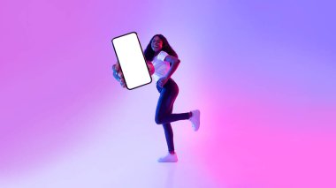 Neşeli genç siyah bir kadın boş bir cep telefonuyla yeni bir uygulamayı tanıtıyor. Sahne canlı neon ışıkları içeriyor. Canlı bir ortam yaratıyor. Reklam için mükemmel..