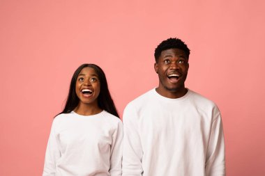 İki mutlu Afro-Amerikan aşığı, bir erkek ve bir kadın, eşleşen beyaz kazaklar giyer ve heyecanla yukarı bakarlar. Parlak pembe stüdyo arka planı onların neşeli ifadelerini geliştirir..