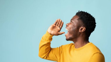 Mavi stüdyo arka planında poz veren mutlu Afrikalı Amerikalı adam, el ele tutuşup yüksek sesle bir şeyler söylüyor, kopya alanı olan bir panorama. Yakışıklı genç siyahi adam duyuru yapıyor, yan görüş.