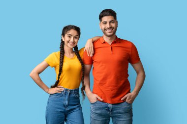 İki genç yetişkin yan yana duruyor, gündelik giysiler içinde gülümsüyor. Erkek turuncu gömlek giyer ve kadın sarı bluz giyer. Neşeli ifadeleri neşeli bir atmosfer yaratıyor..