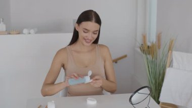 Bir kadın cilt bakımına odaklanır, parlak ve havadar bir banyoya ürün uygular. Doğuştan gelen ışıkla kendine bakmaktan zevk alırken gülümsüyor..