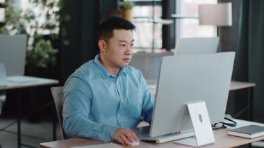 Genç bir adam, çağdaş bir ofisteki gösterişli bir masada işine odaklanır. Doğal ışık odayı dolduruyor, bilgisayar kullanırken konsantrasyonunu vurguluyor..