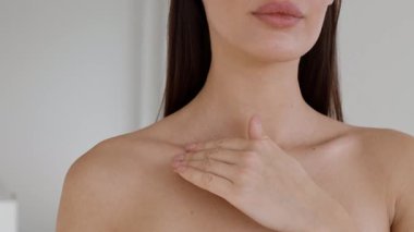 Bir kadın kapalı bir alanda duruyor, bir eliyle yavaşça köprücük kemiğine dokunuyor. Doğal ışık, sıcak atmosferi güçlendirir. Derisini ve rahatlamış ifadesini vurgular..