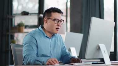 Odaklanmış bir adam iki bilgisayar kullanarak çağdaş bir ofiste masa başında oturuyor. Güneş ışığı büyük pencerelerden girer ve görevleri için verimli bir atmosfer yaratır..