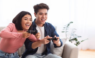 Birlikte oynuyoruz. Heyecanlı Asyalı çift evdeki koltukta oturmuş video oyunları oynuyor, hafta sonları eğleniyorlar. Bilgisayar Oyunları, İki Kişilik Aile İçin Video Oyunları, Hafta sonu Boş Konsepti