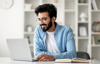 Ağ Kavramı. Bilgisayarda interneti kolaçan eden yakışıklı Hintli genç, Gözlüklü Mutlu Doğulu Adam, İç Ofiste oturuyor, çalışıyor ya da çalışıyor,