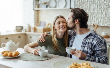 Yüzlerce yıldır gülümseyen beyaz koca, sakallı sarılıp karısını yanağından öpüyor ve modern mutfak içinde kahve içiyor. Boş zaman, içkili kahvaltı ve evde günaydın.