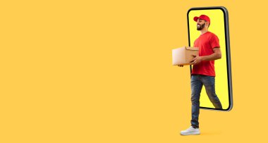 Smartphone Screen 'den çıkan Orta Doğulu kurye. Sarı Stüdyo Arkaplanı' na paket teslim ediyor. Teslimat Başvurusu Konsepti. Panorama, Boş Alan