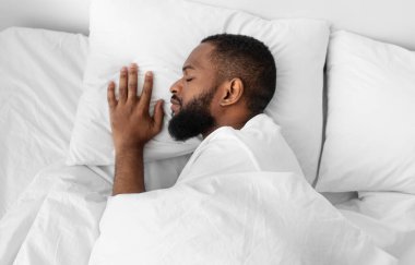 Sakin, sakallı, beyaz yatakta, yatak odasındaki yorganın altında yumuşak yastıkta uyuyan Afro-Amerikan bir adam. Sağlıklı bir uyku çeken, geceleri, hafta sonları ya da tatillerde dinlenen bir adam.