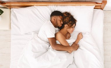 Afro-Amerikan çiftler yatakta uyuyup sarılıyorlar, aşk ve şefkat kavramı, üst bakış açısı.