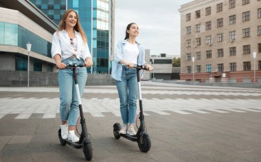 En iyi iki kız arkadaşın şehir merkezinde siyah motorlu scooterlar sürerken, hafta sonları boş zamanlarında gülümseyen iki genç kızın vücut boyu fotoğrafı.