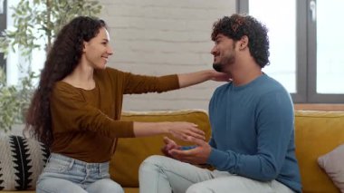 Parlak bir oturma odasında oturan bir çift. Birbirlerine gülümsüyorlar, birbirlerine eşlik ederken sıcak bir sohbet ediyorlar. Sıcak atmosfer bağlantılarını vurguluyor..