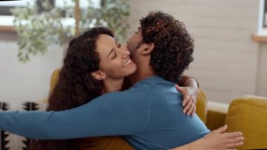 Bir çift, güneş ışığıyla dolu rahat bir oturma odasında sıcak bir kucaklaşmayı paylaşıyor. Yumuşak mobilyalar ve yeşilliklerle çevrili, yakınlıklarını arttıran huzurlu bir anın tadını çıkarıyorlar..