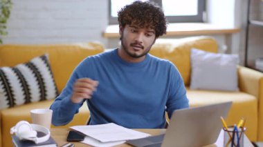 Genç bir adam parlak bir ev ofisinde ahşap bir masada oturuyor. Bilgisayarına odaklanmış. Evrak işleri ve bir fincan kahveyle çevrili. Parlak sarı kanepe ortama sıcaklık katıyor..