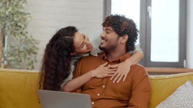 Bir çift rahat bir kanepede oturur ve bir anlık neşeyi paylaşır. Kadın erkeği sevgiyle kucaklarken, o da ona gülümsüyor..