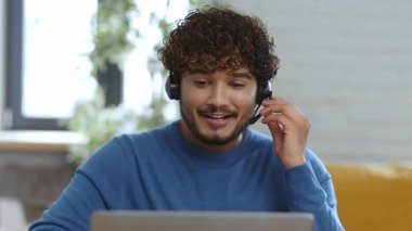 Genç bir erkek, ofisinden sanal bir toplantıya katılıyor. Kulaklık takıyor ve başkalarıyla konuşurken gülümsüyor. Sıcak ve parlak bir atmosfer onu sarıp, bağlantısını güçlendiriyor..