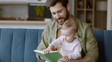 Neşeli bir baba, parlak bir oturma odasındaki mavi bir kanepede bebeğiyle kaliteli vakit geçirir. Renkli bir kitabı keşfederler, bu beslenme anında özel bir bağ kurarlar..