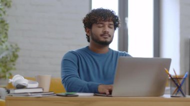 Bir erkek, ahşap bir masada oturur ve dizüstü bilgisayarına konsantre olur. Kitaplar, bir fincan ve ofis malzemeleriyle çevrili halde, doğal ışıkla dolu parlak ve havadar bir çalışma alanının tadını çıkarıyor..