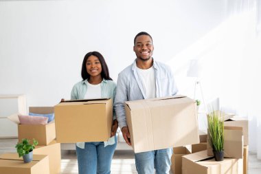 Yer değiştirme konsepti. Mutlu Afro-Amerikan çifti yeni eve karton kutular taşıyor, gülümsüyor ve kameraya bakıyor emlak ve genç aile konutları