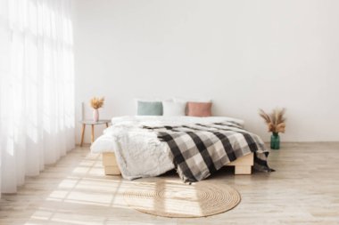 Minimalist çağdaş boho tasarımı. Yastıklı yatak ve battaniyeli masa vazolarda kurumuş bitkiler, yerde yuvarlak halı, büyük perdeli pencere, beyaz duvarlı arka plan, kopyalama alanı, kimse