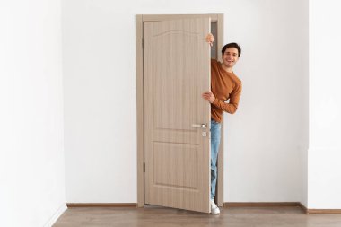 Genç bir adam modern dairesinin kapısında duruyor, bir ziyaretçiyi selamlarken gülümsüyor. Dost canlısı ve misafirperver görünüyor, bin yıllık ev sahibinin ruhunu somutlaştırıyor..