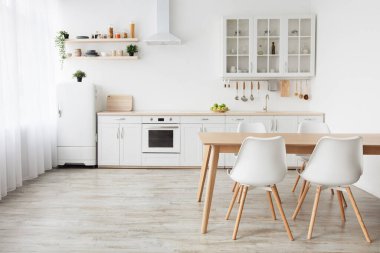 İskandinav iç mimarisi. Mutfak mobilyaları, mutfak eşyaları, sandalyeli yemek masası, bulaşıklı raflar ve pencerenin yanındaki beyaz buzdolabı, boş alan.