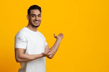 Beyaz tişörtlü yakışıklı orta çağ çocuğu sarı stüdyo arka planında reklam için fotokopi alanı gösteriyor. Güzel, izole bir yer öneriyor.