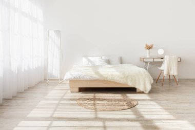 Gerçek fotoğraf, yatak odasının içinde model, basit bir tarz. Yastıklı büyük yatak, gün ışığında ahşap zeminde perdeli halı, kuru bitkilerle dolu masa, beyaz arka planda mobilya.