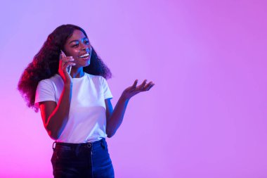 Mutlu bir milenyum siyahi kadın canlı neon ışıklarının altında akıllı telefonuyla konuşuyor. Neşeli ve dostane bir konuşma yaparken gülümsüyor, neşeli tavrını sergiliyor..