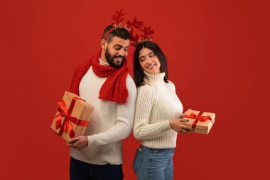 Genç bir ortadoğulu çift canlı kırmızı bir arka plana karşı duruyor, geyik boynuzu takıyorlar..