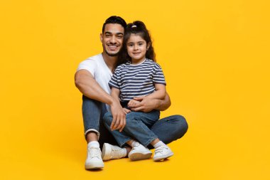 Küçük tatlı kızıyla birlikte mutlu bir Arap babanın portresi stüdyoda sarı arka planda poz veriyor, Orta Doğulu baba ve bayan çocuk kameraya sarılıyor ve gülümsüyor, uzayı kopyalıyor.