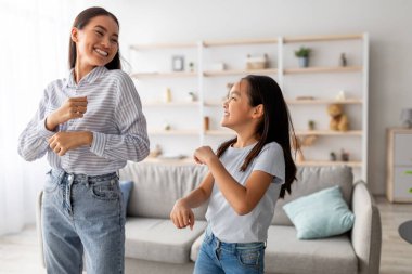 Heyecanlı Asyalı anne ve tatlı kız müzik eşliğinde dans edip evde eğleniyorlar, birbirlerine gülümsüyorlar. Genç anne ve çocuğu oynaşıyor ve en sevdiği şarkının tadını çıkarıyorlar.