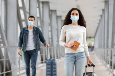 Yeni Normal. Havaalanı Terminali 'nde, erkek ve kadın yolcuların Coronavirus salgınında seyahat ederken, havaalanına giderken yanında tıbbi maske takan genç adam ve kadının portresi.