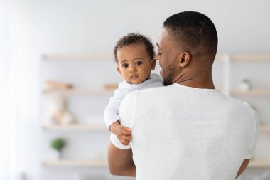 Baba sevgisi. Siyah milenyum adamı, elinde sevimli bir bebekle evin içinde poz veriyor, Afrikalı Amerikalı babayı seviyor, tatlı bebeğini kucağında tutuyor, küçük çocuk kameraya bakıyor, mekanı kopyalıyor.