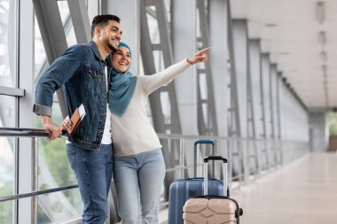 Havalimanında bavullarını taşıyan neşeli Müslüman çift, terminalde bekleyen mutlu Orta Doğulu eşler, havalanmadan önce birlikte vakit geçiriyorlar.