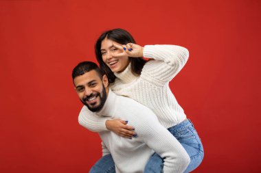 Neşeli bir Arap çifti birlikte neşeli bir anın tadını çıkarır. Adam, kız arkadaşı barış işareti ile poz verirken onu sırtında taşıyor. Belli ki canlı kırmızı bir arka planda eğleniyorlar..