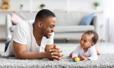 Baba Bebek Bağlantısı. Mutlu siyahi adam evde tatlı çocukla kaynaşıyor, Afrikalı Amerikalı baba ve sevimli çocuğu oturma odasında yerde dinleniyor, boş yer var.