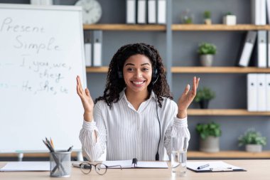 Çevrimiçi öğretmenlik, uzaktan öğrenme veya öğretme, yakınlaşma dersi, video çağrısı, uzaktan eğitim ve yeni normal, covid-19. Webcam görüntüsü. Bin yıllık gülümseyen kulaklıklı zenci kadın kuralları ve jestleri açıklıyor.