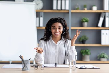 Pozitif öğretmen, öğretmen internetten uzaktan ders, eğitim, sanal webinar, covid-19 için arama yapıyor. Kulaklık takan neşeli siyah kadın oturma odasının iç tarafındaki kameraya bakıyor.