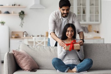 Hoş bir sürpriz ve yıl dönümü hediyesi, evde tek başına geçirilen tatili kutlamak için. Mutlu çekici Arap adam karısına doğum gününde ya da sevgililer gününde oturma odasında hediye verir.