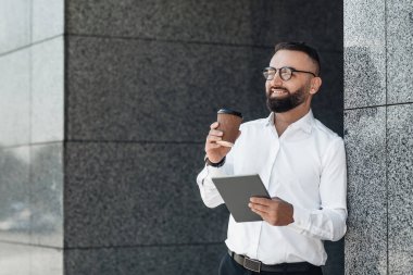 Olgun iş adamı dijital tablet kullanıyor ve kahve içiyor. Mola verip dışarıda dinlenirken boş zamanlarının tadını çıkarıyor. Kitap okuyor ya da sosyal medyayı kontrol ediyor.