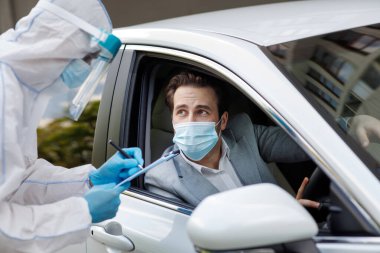 Yolcuları ve sürücüleri kontrol eder, biyolojik kıyafetli adam tablet, COVID-19 karantina, ilaç ve sağlık hizmetlerine veri yazar. Korumalı maskeli bir erkek arabada koronavirüs testi bekliyor.