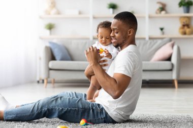 Babalar Bakımı. Genç siyahi adam, sevimli küçük oğluyla evde vakit geçiriyor, Afrikalı Amerikalı babayı seviyor, sevimli bebek bebekle oturma odasında oynuyor, babalığının tadını çıkarıyor, boşluğu kopyalıyor.