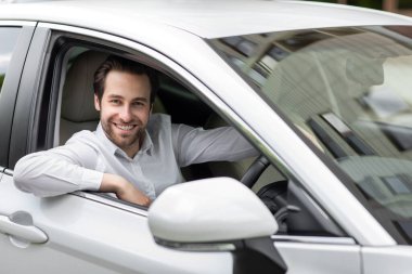 Gülümseyen genç adamın portresi, sabah işe gidip gelirken kendi arabasını sürüyor. Milenyum Çekici, tişörtlü mutlu Avrupalı adam beyaz arabada oturur, kameraya bakar, boş alan, maket