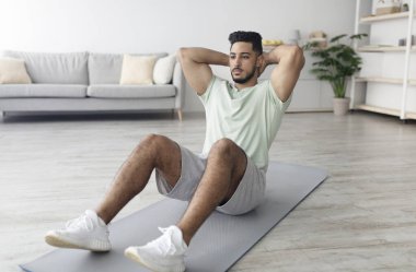 Yoga minderi üzerinde egzersiz yapan yakışıklı genç bir Arap. Evde karın kaslarını güçlendiriyor. Uzayı kopyalıyor. Orta Doğulu adam kapalı alanda salgın sırasında formda kalıyor. Yerli fitness konsepti