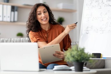 Genç profesyonel öğretmen, blogu için bilgisayar ekranını kullanarak ve ona bakarak video dersi kaydediyor. Kalemi beyaz tahtaya formüllerle doğrultuyor. Çevrimiçi okul, bilgi. Öğretmenine odaklan. E-öğrenme