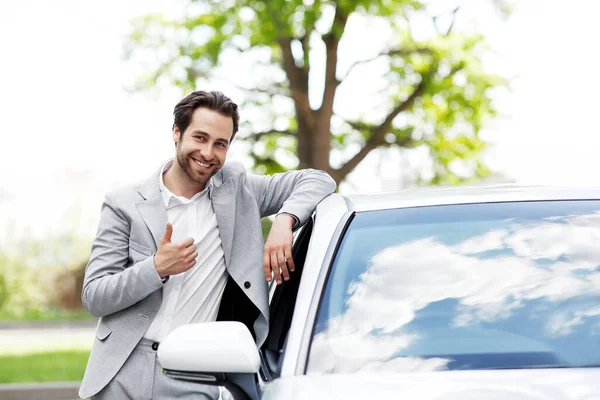 Mükemmel kalitede bir araba, onay, otomobil blogu ve galeride çalışma. Modern yeni ulaşım aracının yanında kirli sakallı, neşeli, beyaz bir adam, baş parmağını gösteriyor, satın almayı onaylıyor, açık havada