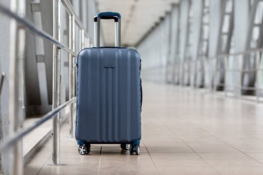 Boş havalimanında duran şık kabin valizinin yakın plan fotoğrafı, mavi el çantası terminalde bekliyor, reklam afişi ve uçak biletleri için, kopyala