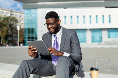 Mutlu Afro-Amerikan isyancı ajanı tablet üzerinde çalışıyor, bloknotlarda haberlere bakıyor, şehir merkezindeki modern ofis merkezinin yakınında oturuyor,